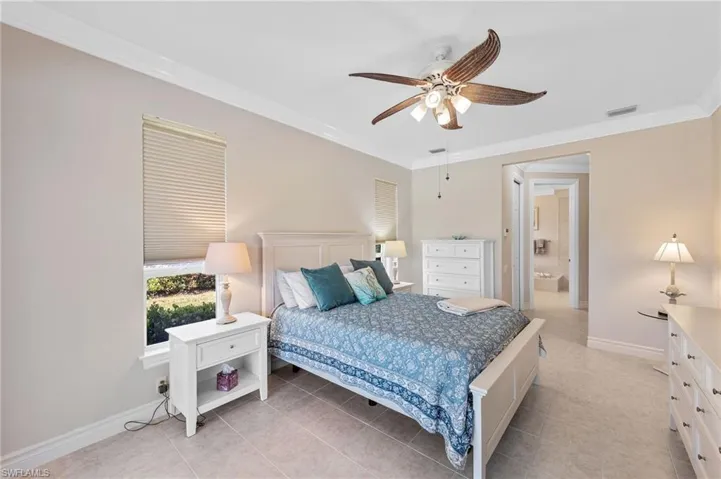 Bedroom featuring crown molding, ceiling fan, light tile patterned floors, and ensuite bath