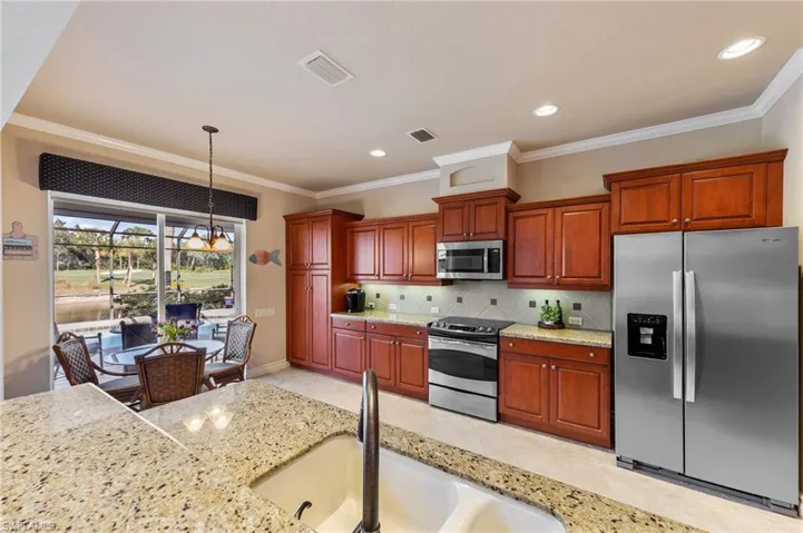 Kitchen featuring appliances with stainless steel finishes, light stone counters, ornamental molding, hanging light fixtures, and decorative backsplash