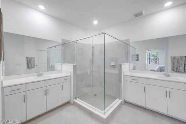 Full bathroom with a shower stall, two vanities, tile patterned flooring, and recessed lighting