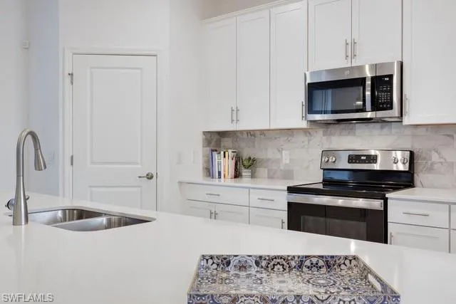 Kitchen with stainless steel appliances, a sink, light countertops, backsplash, and white cabinetry