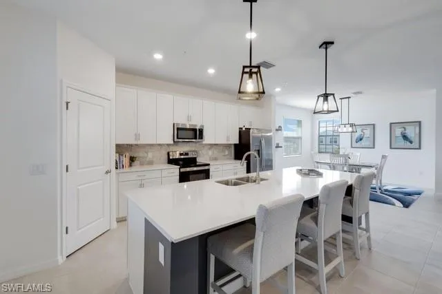 Kitchen with stainless steel appliances, a sink, a large island, decorative backsplash, and white cabinets