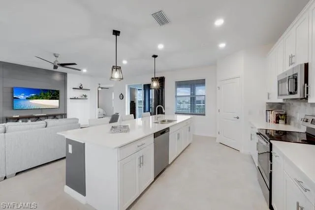 Kitchen with stainless steel appliances, a sink, open floor plan, light countertops, and white cabinetry