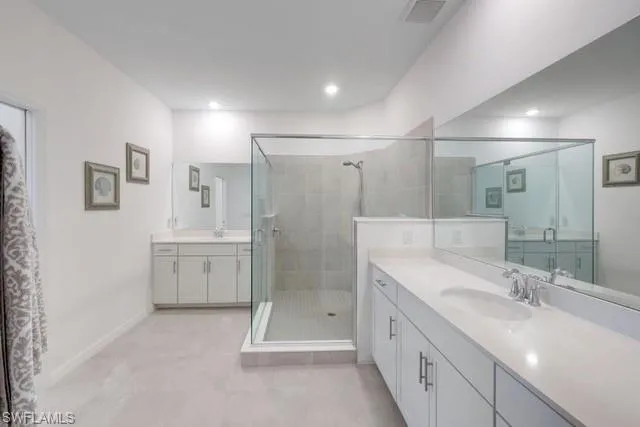 Full bathroom featuring a shower stall, two vanities, baseboards, and recessed lighting