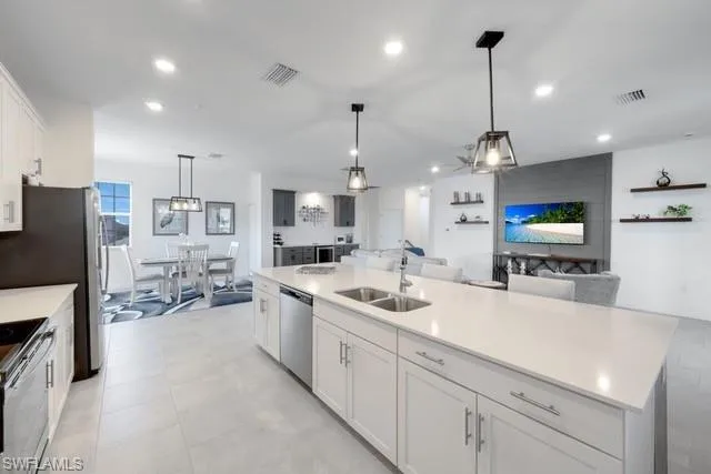 Kitchen featuring appliances with stainless steel finishes, a sink, light countertops, hanging light fixtures, and white cabinets