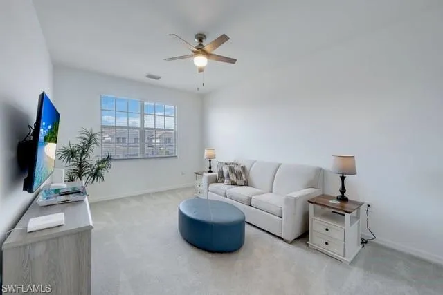 Carpeted living room with a ceiling fan and baseboards