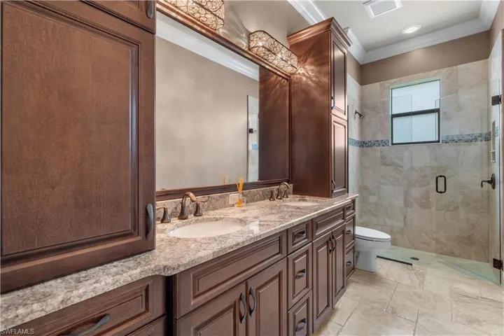 Bathroom with an enclosed shower, tile patterned flooring, crown molding, toilet, and dual bowl vanity