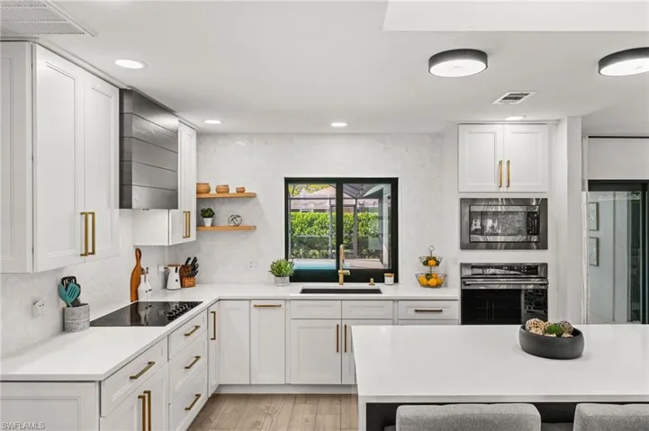 Kitchen with stainless steel appliances, white cabinets, light stone counters, light wood-type flooring, and open shelves