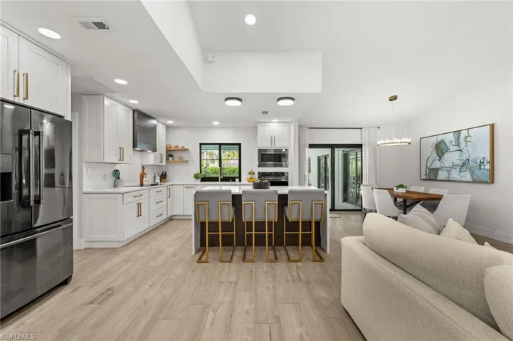 Kitchen with a breakfast bar area, a kitchen island, white cabinetry, stainless steel appliances, and light wood-type flooring