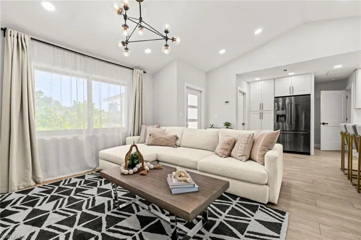 Living room with light wood finished floors, lofted ceiling, and suspended lighting
