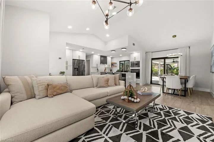 Living room with a chandelier, light wood-type flooring, and lofted ceiling