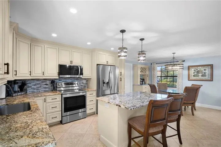 Kitchen with cream cabinetry, stainless steel appliances, light stone countertops, a kitchen breakfast bar, and a center island