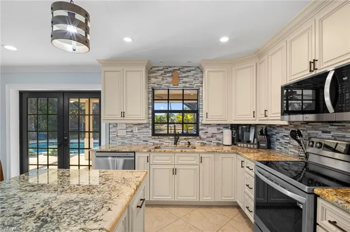 Kitchen featuring stainless steel appliances, cream cabinets, french doors, light stone countertops, and backsplash