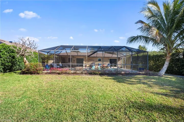 Rear view of property featuring a sunroom, a swimming pool, glass enclosure, and a lawn