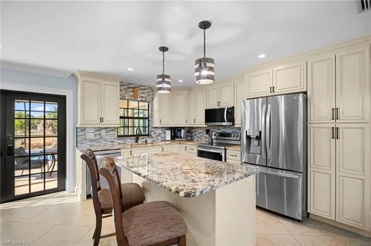 Kitchen with cream cabinets, stainless steel appliances, light stone counters, a center island, and crown molding
