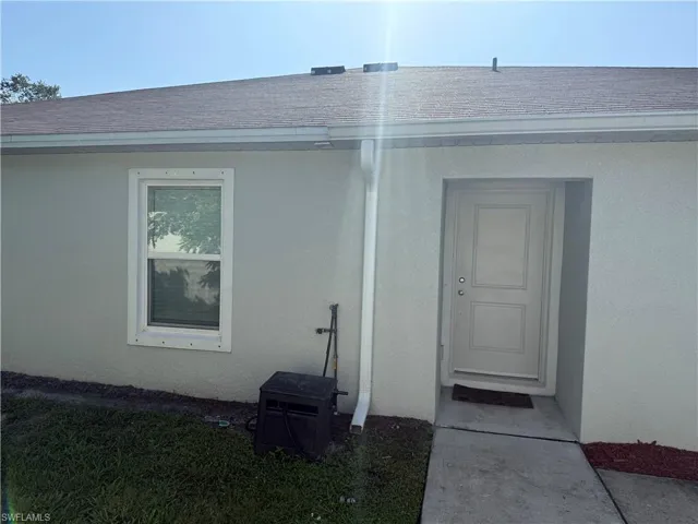 Property entrance featuring stucco siding and roof with shingles