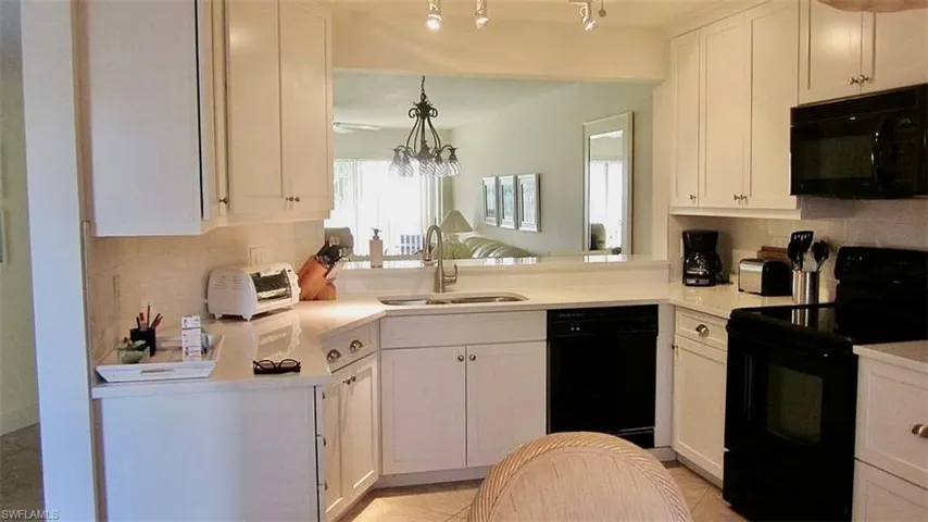 Kitchen with black appliances, decorative backsplash, white cabinets, light stone countertops, and light tile patterned flooring