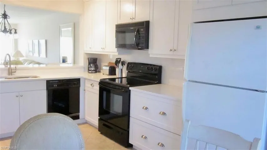 Kitchen featuring black appliances, white cabinets, light tile patterned flooring, hanging light fixtures, and open floor plan