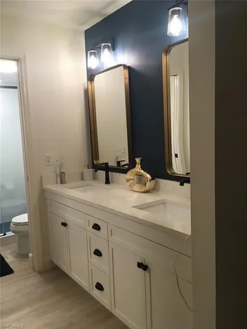 Bathroom with double vanity, a stall shower, and light wood-type flooring