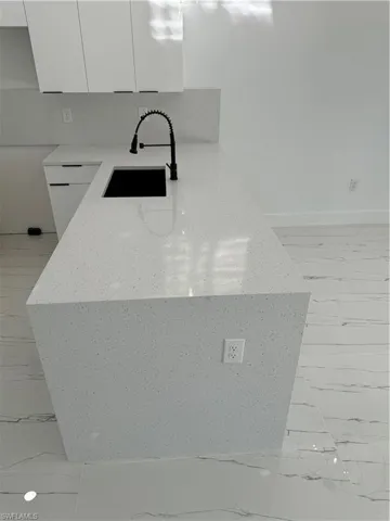 Interior details featuring light stone countertops, sink, kitchen peninsula, and white cabinets