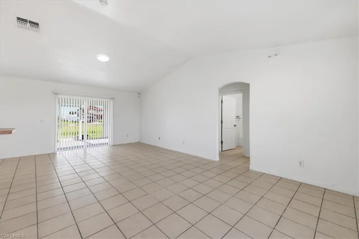 Spacious room featuring tile flooring, vaulted ceiling, and sliding glass doors with vertical blinds