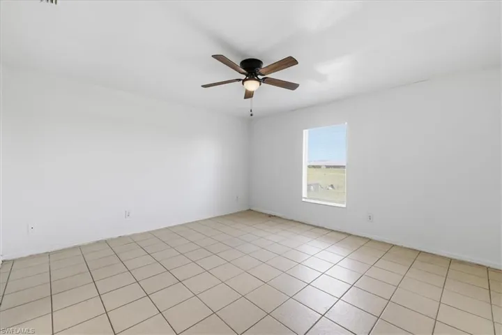Spacious room featuring neutral-toned tile flooring, a contemporary ceiling fan with integrated lighting, and a single window