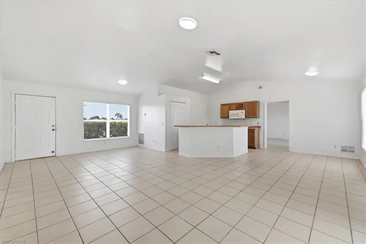 Spacious open-concept living area featuring light-toned tile flooring, vaulted ceilings, and recessed lighting