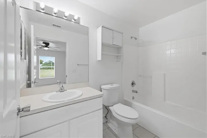 Bathroom featuring a white vanity with an integrated sink, a large wall-mounted mirror, overhead vanity lighting, a white toilet, and a combination tub/shower with white subway tile surround