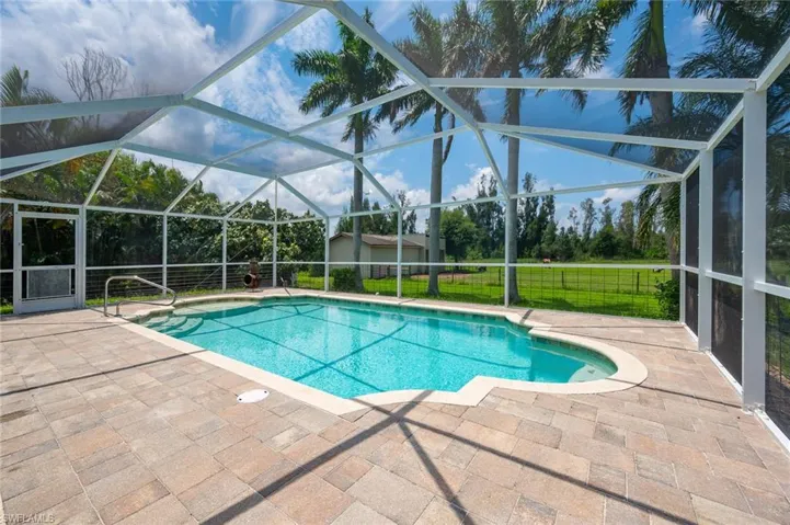 View of pool featuring glass enclosure, a patio, and a lawn