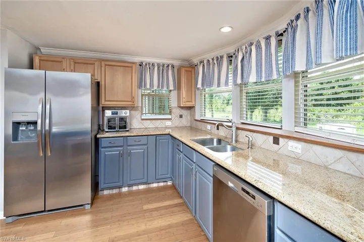 Kitchen featuring light wood-type flooring, appliances with stainless steel finishes, light brown cabinetry, sink, and decorative backsplash