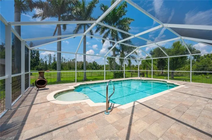 View of pool with glass enclosure, a patio area, and a yard