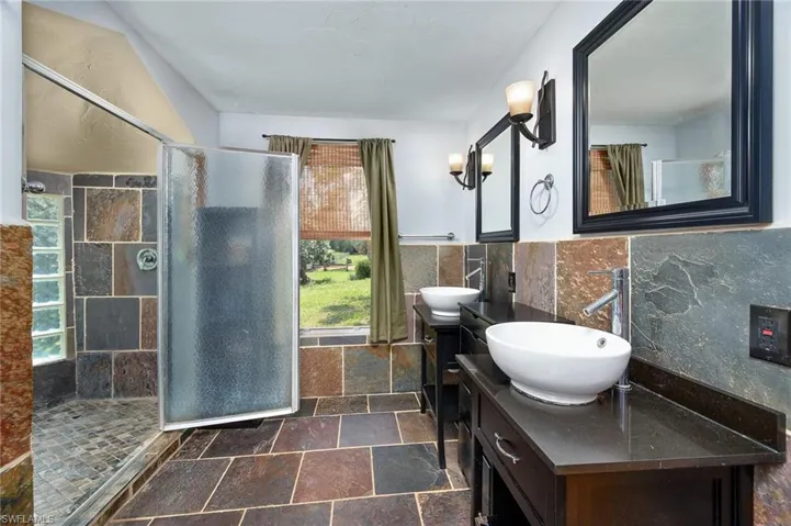 Bathroom featuring tile patterned flooring, backsplash, tile walls, dual bowl vanity, and tiled shower