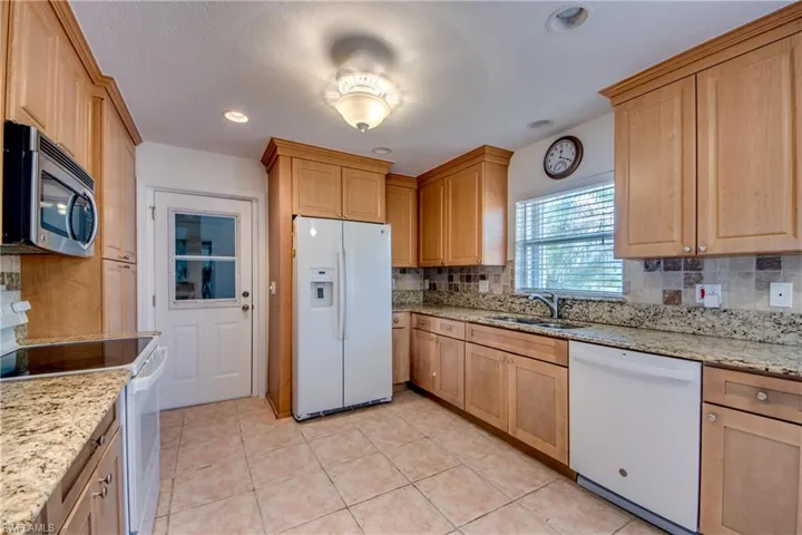 Kitchen featuring light tile patterned flooring, white appliances, sink, light stone countertops, and backsplash