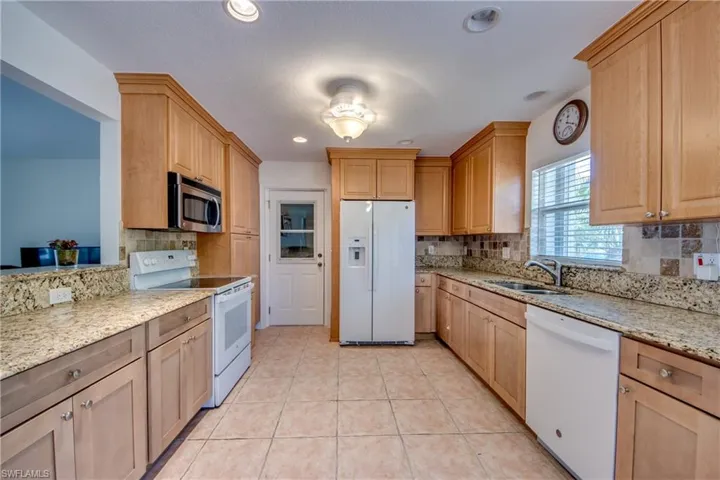 Kitchen with white appliances, sink, light stone countertops, light tile patterned floors, and backsplash