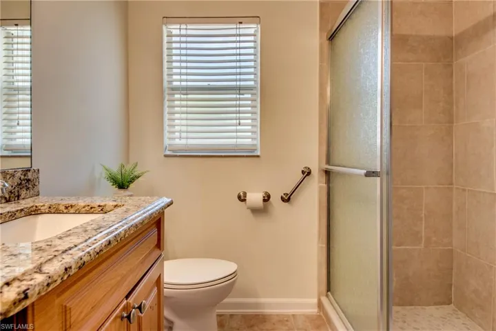 Bathroom with a shower with shower door, tile patterned floors, toilet, and vanity