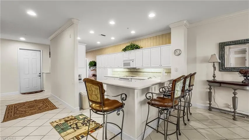 Kitchen featuring white appliances, white cabinets, crown molding, light tile patterned floors, and tasteful backsplash