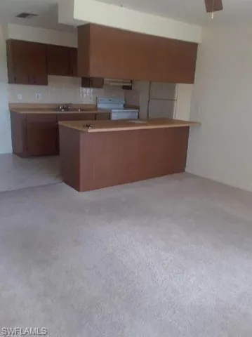 Kitchen with a peninsula, white range with electric stovetop, light countertops, and wood finish cabinets