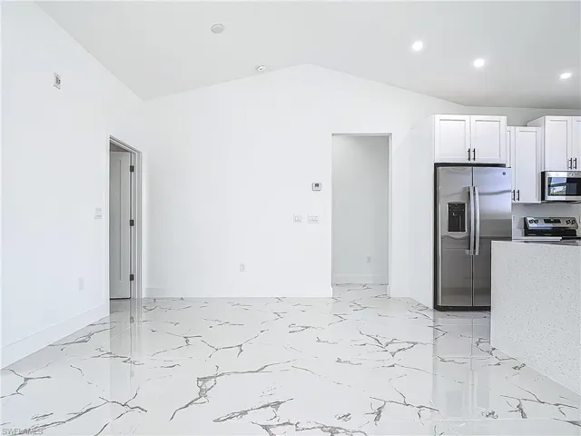 Kitchen with stainless steel appliances, recessed lighting, light marble finish floors, white cabinets, and vaulted ceiling