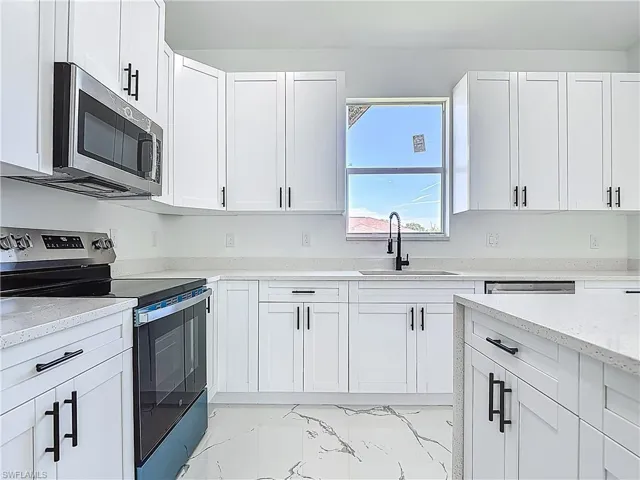 Kitchen with stainless steel appliances, a sink, white cabinets, light marble finish flooring, and light stone counters