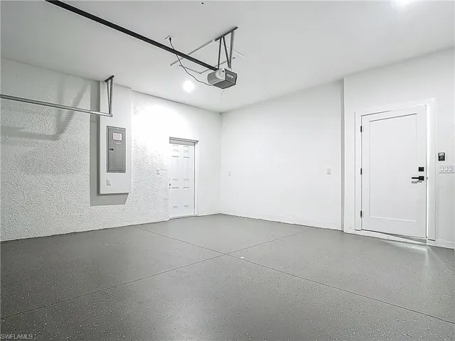 Garage featuring a garage door opener, electric panel, and a textured wall