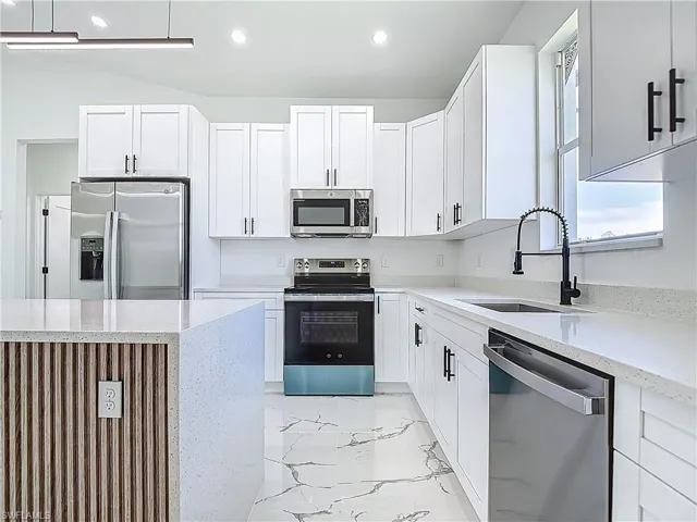 Kitchen with appliances with stainless steel finishes, a sink, light marble finish flooring, white cabinets, and recessed lighting