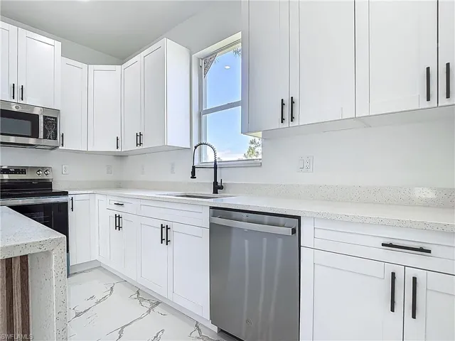 Kitchen featuring stainless steel appliances, a sink, light marble finish flooring, and white cabinetry