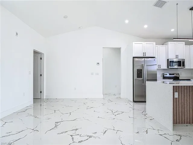 Kitchen with appliances with stainless steel finishes, light marble finish floors, white cabinetry, lofted ceiling, and recessed lighting