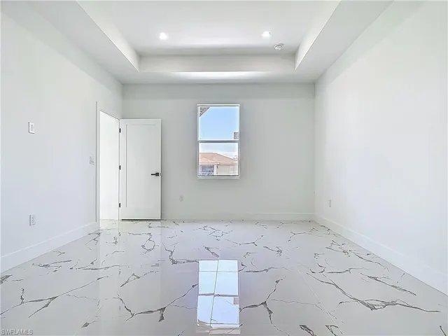 Spare room with a tray ceiling, baseboards, light marble finish floors, and recessed lighting