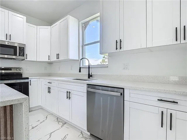 Kitchen with appliances with stainless steel finishes, a sink, light marble finish floors, and white cabinets