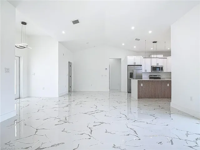 Unfurnished living room featuring recessed lighting, vaulted ceiling, light marble finish floors, and baseboards