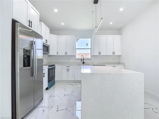 Kitchen featuring appliances with stainless steel finishes, light marble finish flooring, white cabinetry, light countertops, and recessed lighting