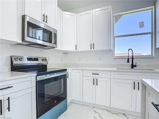 Kitchen with appliances with stainless steel finishes, a sink, light marble finish floors, white cabinets, and light stone counters