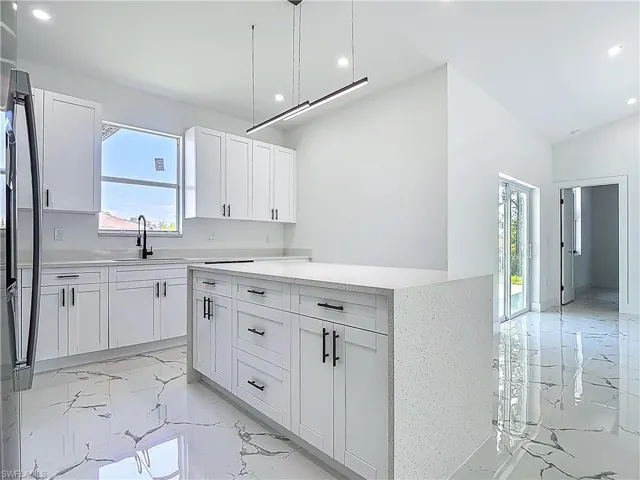Kitchen with a sink, light marble finish flooring, recessed lighting, white cabinets, and a center island