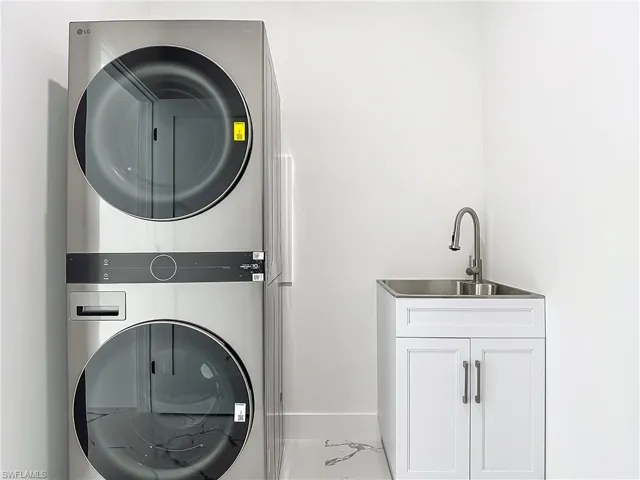 Laundry room featuring stacked washing machine and dryer, cabinet space, marble look tiles, and baseboards