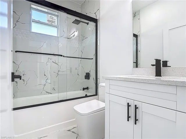 Bathroom with toilet, bath / shower combo with glass door, and vanity